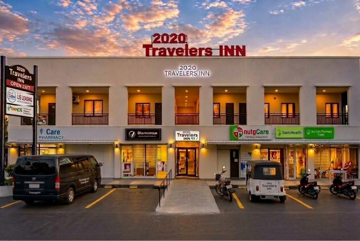 Exterior of 2020 Travelers Inn in Dumaguete City at dusk, with the rooftop sign, entrance ramp, and parked tricycles